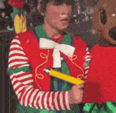 a man in a clown costume is holding a yellow pencil in front of a stuffed animal .