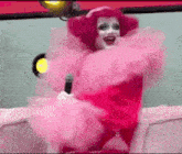 a drag queen is sitting on a couch holding a microphone .