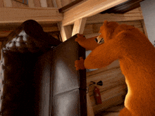a brown bear is standing next to a brown couch and a red fire extinguisher
