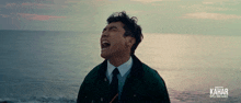 a man in a suit and tie is screaming in front of the ocean with kahar written on the bottom