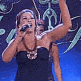 a woman in a black dress is singing into a microphone with her arm in the air .