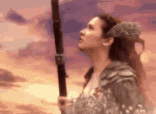 a woman with horns is holding a spear in the desert