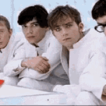 a group of young men wearing white jackets and glasses are sitting together