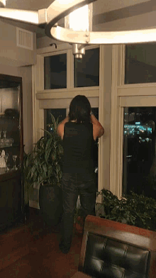 a woman in a black shirt stands in front of a window looking out