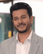 a man with a beard wearing a suit and white shirt smiles for the camera