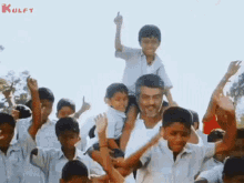 a man is carrying a boy on his shoulders while a group of children are raising their hands in the air .
