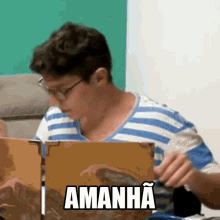 a man in a blue and white striped shirt is reading a book with the word amanha on the front
