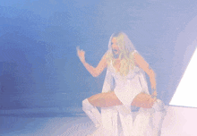 a woman in a white bodysuit and white boots is sitting on a white chair