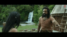 a man with a beard is pointing at a woman in front of a waterfall in a movie .