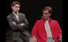 two men are standing next to each other on a stage in a dark room . one of the men is holding a fan .