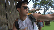 a man wearing sunglasses and a white tank top is pointing to the side