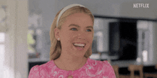 a woman in a pink dress and headband is smiling in a kitchen .