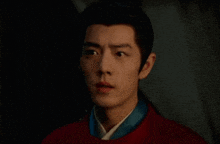 a close up of a man 's face in a dark room wearing a red shirt .