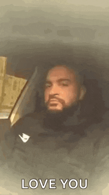 a man with a beard is sitting in the back seat of a car with his eyes closed and says `` love you '' .