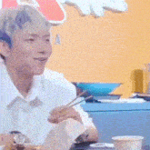 a young man is sitting at a table with chopsticks in his hand .