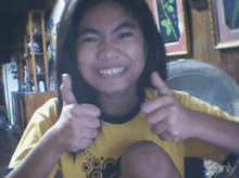 a girl wearing a yellow shirt with a black cat on it gives two thumbs up