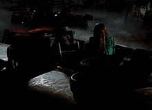 a woman in a green shirt sits in front of a pile of tires in a dark room