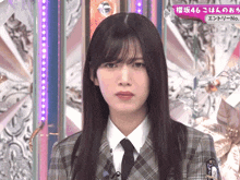 a woman wearing a plaid jacket and tie looks at the camera with the number 46 on the bottom right