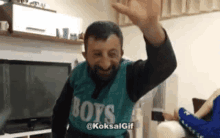 a man in a green shirt that says boys is waving his hand .