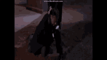 a man in a suit is kneeling down in the dirt while another man holds his hand over his shoulder .
