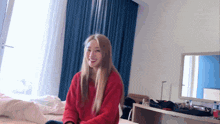 a woman in a red sweater sits on a bed in a room