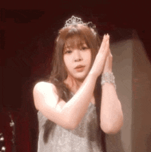 a woman wearing a tiara and a silver dress is clapping her hands together .