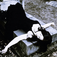 a woman in a black dress is laying on a stone