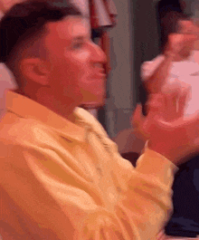 a man in a yellow shirt and tie is clapping his hands in a crowd .