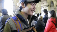 a young man wearing a hat and a backpack is smiling in a crowd of people .