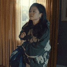 a woman in a green hoodie holds a backpack and looks out a window