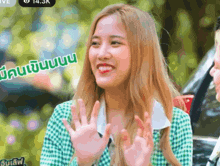 a woman in a green and white plaid shirt is smiling and waving