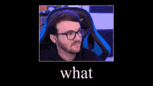 a man with glasses and a beard is sitting in a blue chair with the words `` what '' above him .