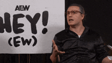 a man in a black shirt stands in front of a sign that says hey ( ew )