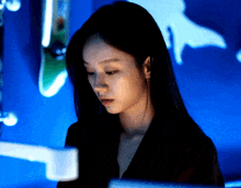 a woman in a dark room with a blue wall behind her