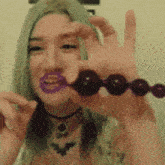 a woman with green hair and purple lipstick is holding a purple toy in her hand .