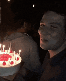 a young man sitting in front of a birthday cake with candles