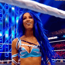 a woman with blue hair is standing in front of a crowd in a wrestling ring and smiling .