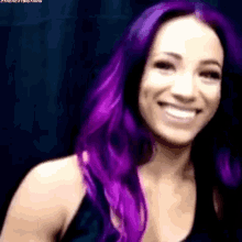 a woman with purple hair is smiling while wearing a black tank top .
