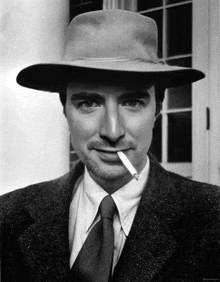 a man with a cigarette in his mouth wearing a hat and tie