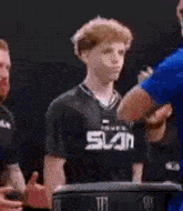 a young man in a black shirt with the word sun on it is standing in front of a group of men .