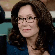 a woman wearing glasses and a blue jacket looks to the side