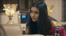 a woman in a sari is sitting at a table with a bottle of wine in front of her .