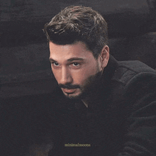 a man with a beard wearing a black jacket is looking down
