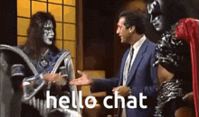 two kiss singers are talking to a man in a suit and tie in a room .