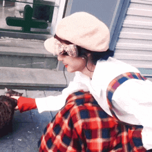 a woman wearing a hat and plaid skirt is petting a cat on the sidewalk