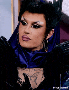 a close up of a drag queen 's face with a butterfly tattoo on her chest