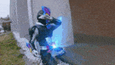 a person in a superhero costume is standing in front of a brick wall holding a blue object .