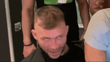 a group of men are standing around a man in a black shirt who is making a funny face