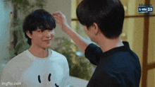 a man is touching another man 's head while they are standing next to each other .