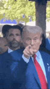 a man in a suit and tie is pointing at the camera while another man stands behind him .